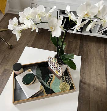 Reviewer photo of the green and gold tray holding a vase of orchids on a coffee table