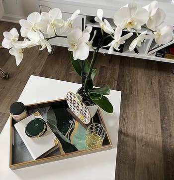 Reviewer photo of the green and gold tray holding a vase of orchids on a coffee table