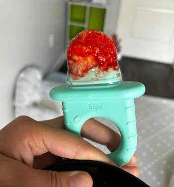 a reviewer holding the feeder with a raspberry smushed inside