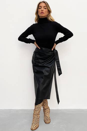 full look of the model wearing the black wrap skirt with boots and a turtleneck