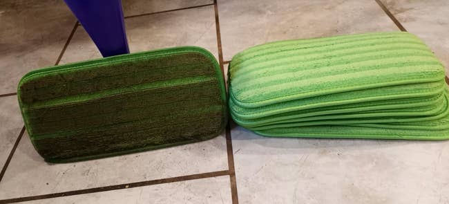 A dirty green mop head on a swiffer next to the clean versions stacked in a pile 