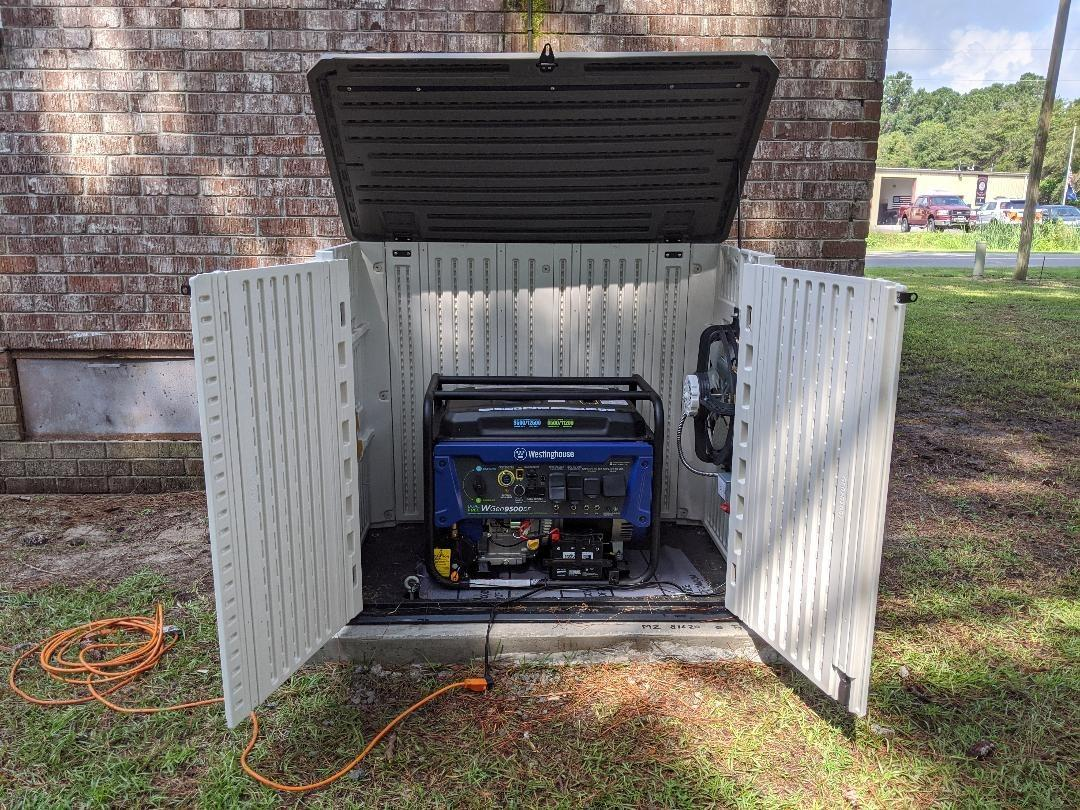 A portable generator is placed inside an open outdoor storage cabinet.