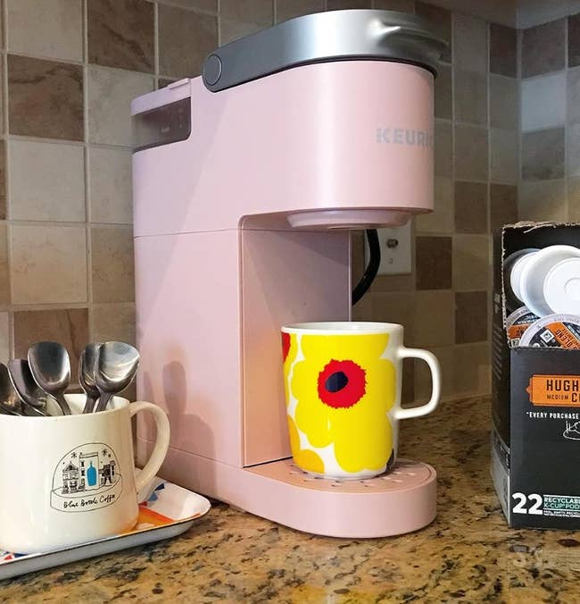 A pastel pink small Keurig on a counter brewing coffee into a mug 