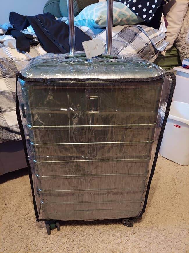 Large suitcase protected with a wide integrative cover, sitting successful a chamber with a furniture and laundry handbasket disposable successful the background