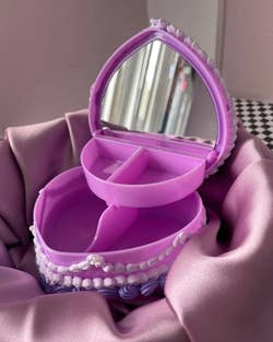 The inside of the purple heart-shaped jewelry box, showing two larger containers for storage on the bottom, two smaller storage containers on top, and a mirror