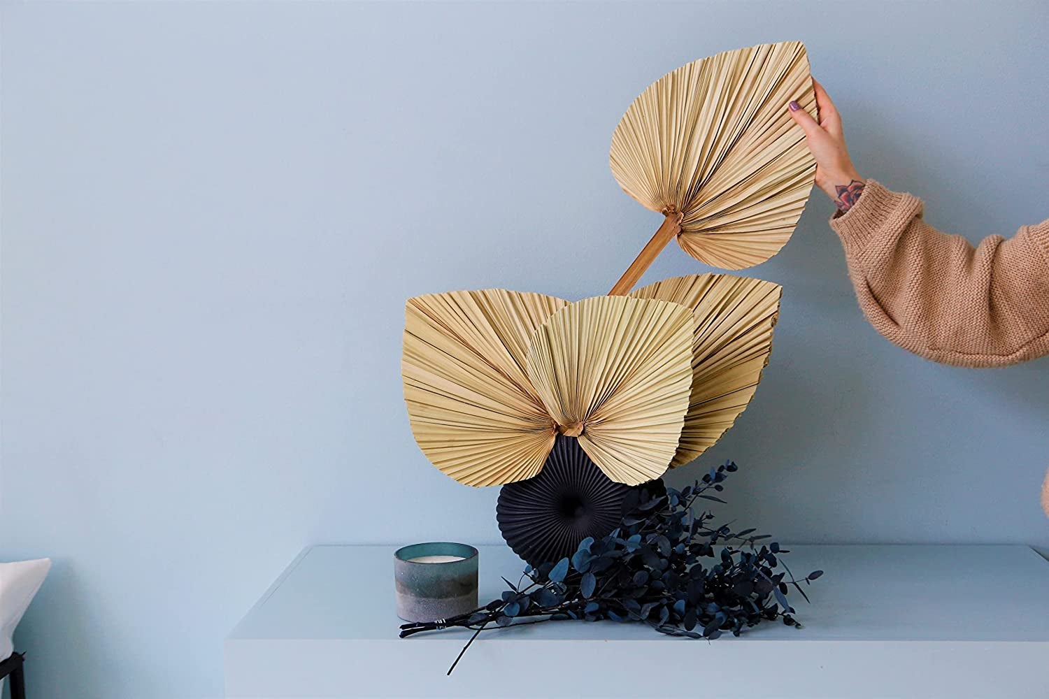 hand grabbing one of four palm fronds from a vase
