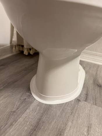Bottom presumption    of a achromatic  toilet, showing its basal  against a woody  floor. The representation  highlights the toilet's installation and design