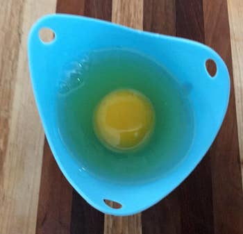 An egg poaching cup with a freshly cracked egg yolk inside