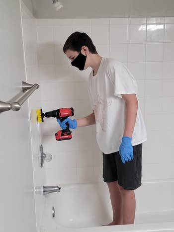 a reviewer's son in the bath tub using the drill brush on the shower wall