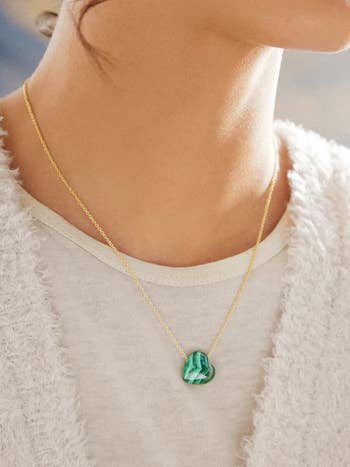 model wearing a simple gold necklace with a green heart pendant