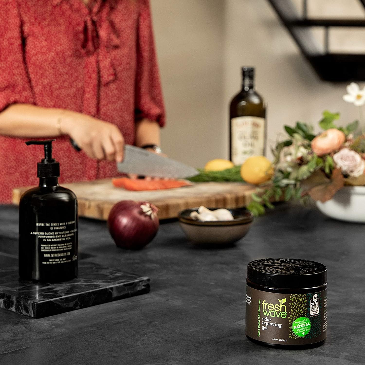 The jar of odor-removing gel on kitchen counter with model chopping food in the background