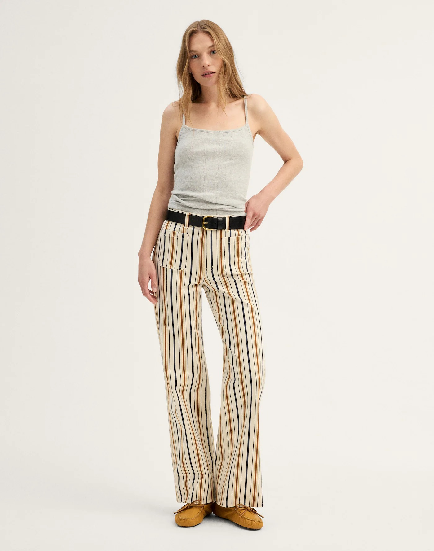 Person wearing a sleeveless top and striped wide-leg pants with a belt, posing for a fashion article