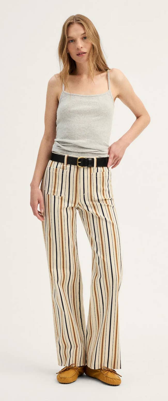 Person wearing a sleeveless top and striped wide-leg pants with a belt, posing for a fashion article