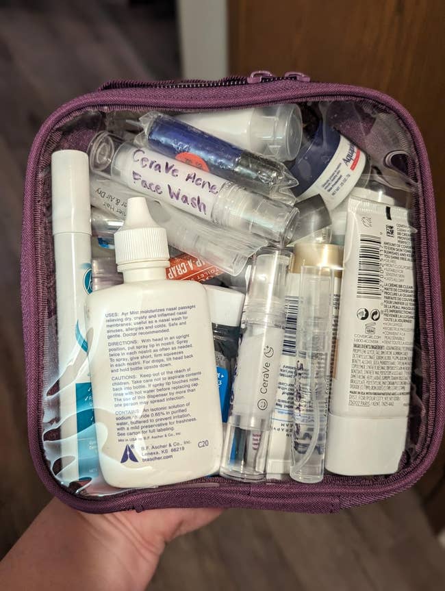 Clear pouch filled with various travel-sized skincare and toiletries, including labeled bottles and tubes for face wash and lotion
