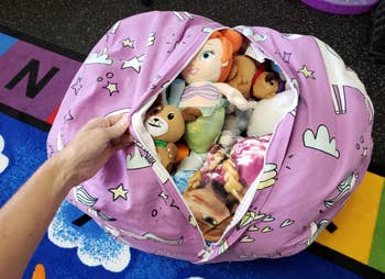 Hand opening a plush toy storage bag with various stuffed animals inside