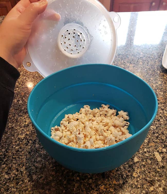 Person holding a popcorn maker lid over a bowl of freshly popped popcorn