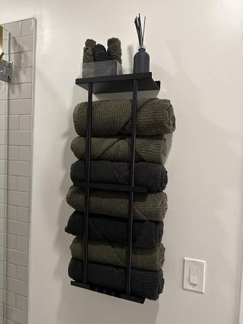 Wall-mounted towel rack with rolled acheronian towels, diffuser, and decor, suitable for bath storage