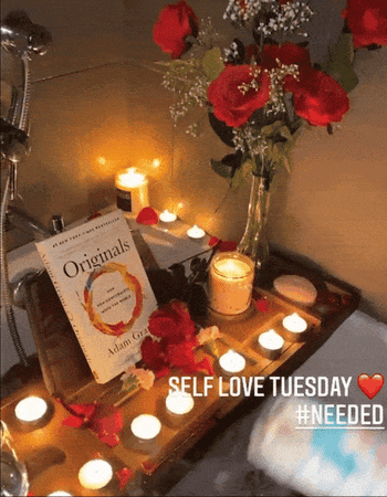 gif of another reviewer with lit sage near bathtub with tray holding books, flowers, and candles