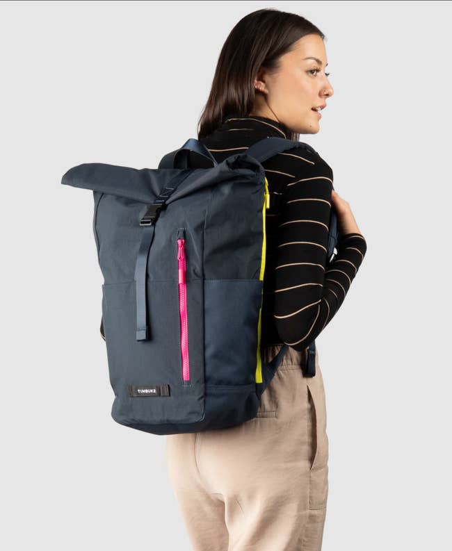 Woman modeling a backpack with a roll-top closure and side zipper