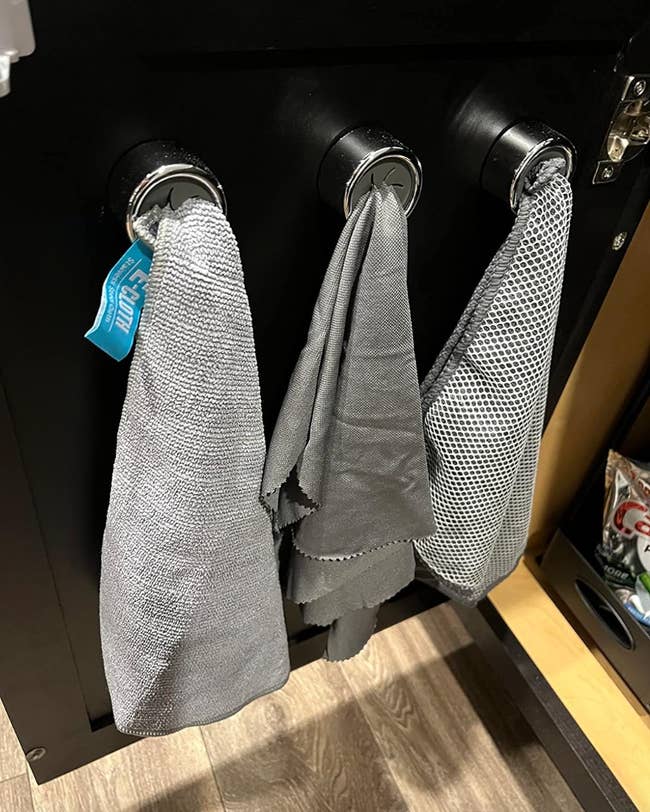 Three kitchen towels hanging on black hooks installed in a kitchen cabinet 
