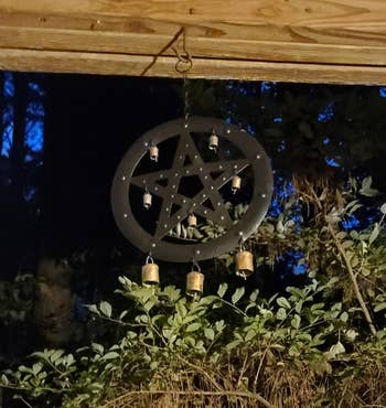 A pentagram wind chime with bells hanging from a wooden beam at night