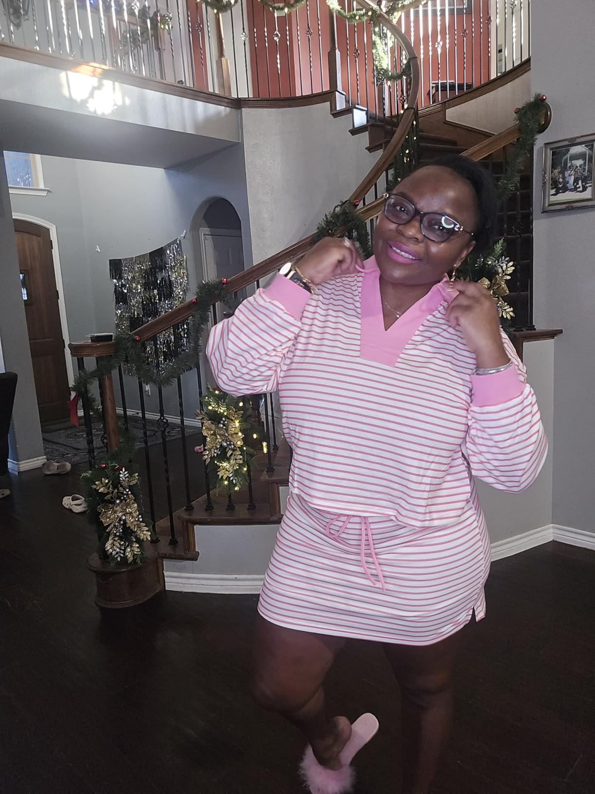 Person posing connected  a staircase, wearing a striped casual formal  with a v-neck and drawstring waist, accessorized with glasses and pinkish  slippers