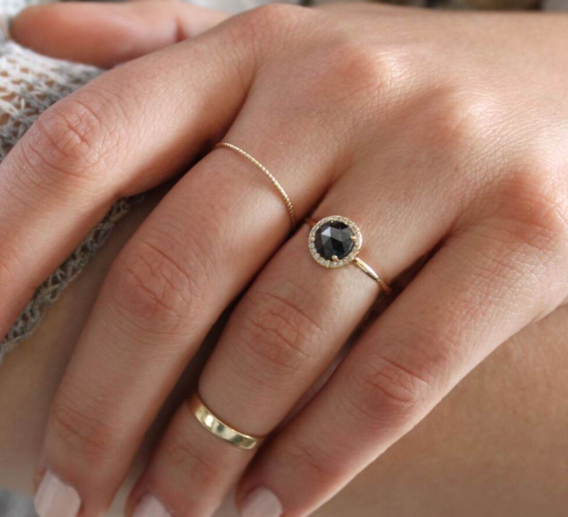 The black diamond ring in a round cut with a halo of diamonds surrounding it and a gold band