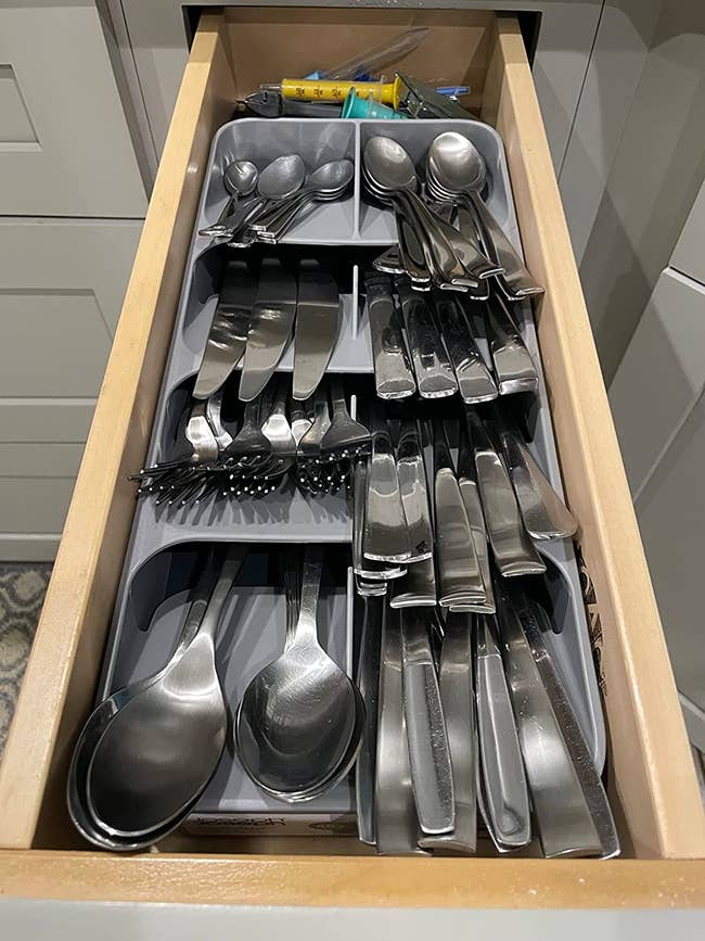 A drawer with the utensil organizer filled with spoons, forks, and knives