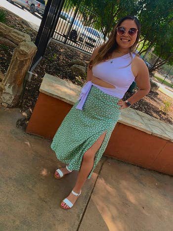 reviewer in a white top and polka-dotted skirt with white sandals posing on a sidewalk