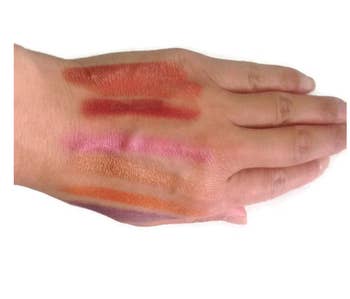 A person's hand with swatches of the makeup