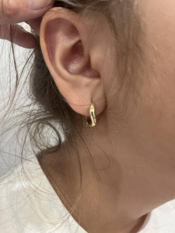 Close-up of a person's receptor wearing a tiny golden hoop earring, showcasing jewelry detail