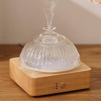 A wooden and glass essential oil diffuser emits steam on a wooden surface, highlighting a soothing and elegant home accessory
