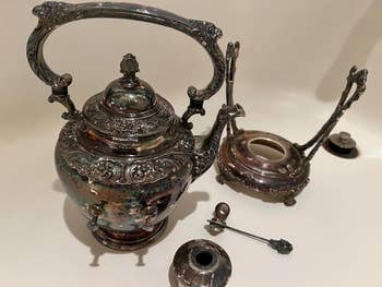 before image of a tarnished Antique tea set including a kettle with intricate designs, a stand, and a burner