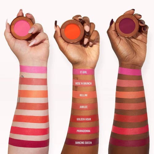 Three arms with different skin tones displaying swatches of various lipstick shades, alongside the corresponding product