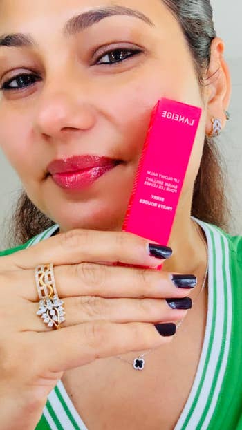 Person holding Laneige articulator balm package, wearing a greenish top, metallic earrings, and reddish lipstick