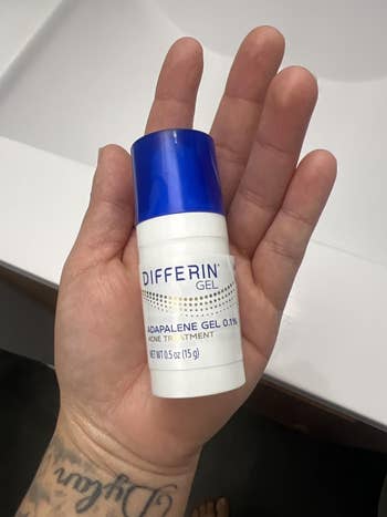 Hand holding a tiny vessel of Differin Gel