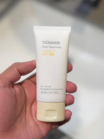 Hand holding a conduit  of Mixsoon Bean Sunscreen SPF 50, emphasizing wide  spectrum extortion  suitable for skincare shopping