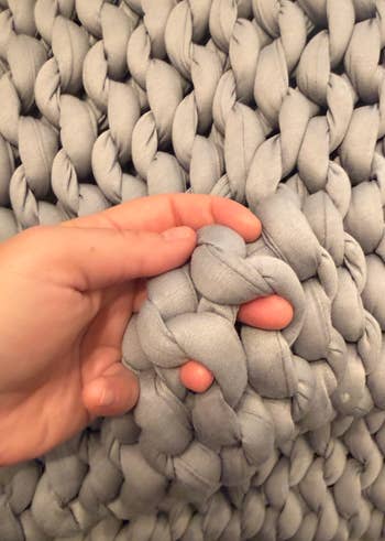 Hand touching a chunky knit blanket, showcasing the thick, woven texture, perfect for cozy location decor