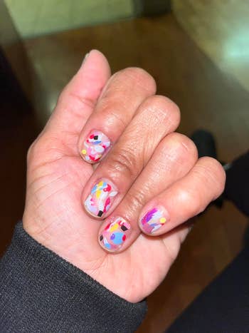 A manus with multicolored abstract nail art, featuring dots and geometric shapes, is shown against a neutral background