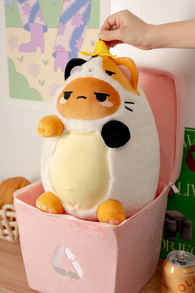 hand pulling plush potato in calico costume out of pink plush bin