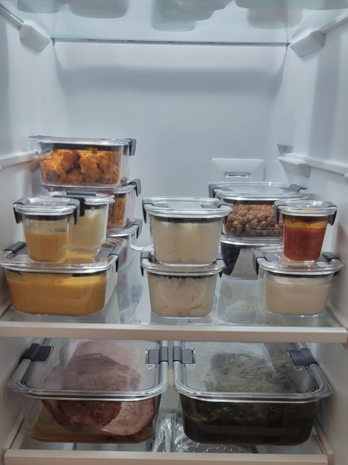 Organized fridge shelves with glass containers holding various foods, including leftovers and sauces, suitable for meal prep or storage