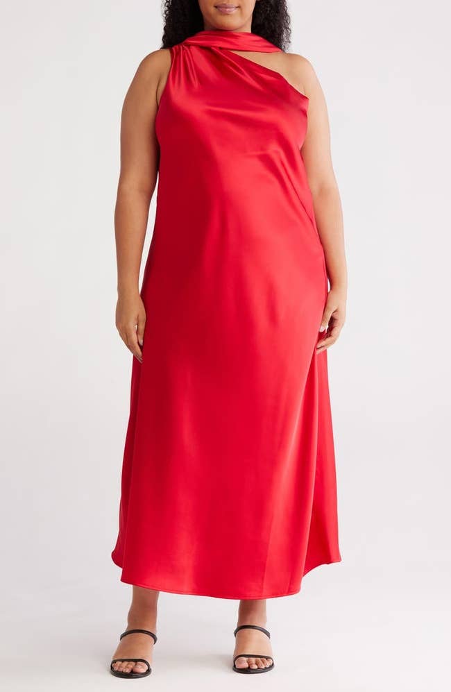 Model wearing a sleeveless, draped, one-shoulder red dress, paired with simple black sandals