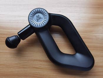 Handheld massage gun with ergonomic design on a wooden surface