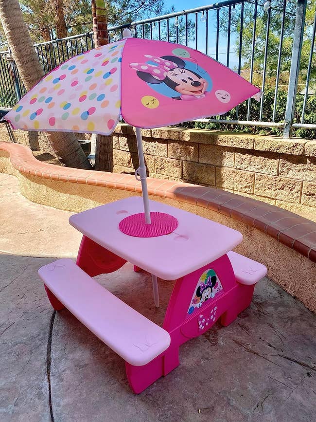 a pink minnie mouse picnic table with an umbrella in the middle
