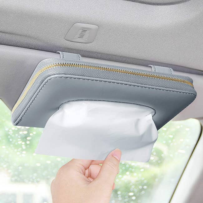 A small gray zippered rectangular pouch attached to a car visor with tissues coming out of it 