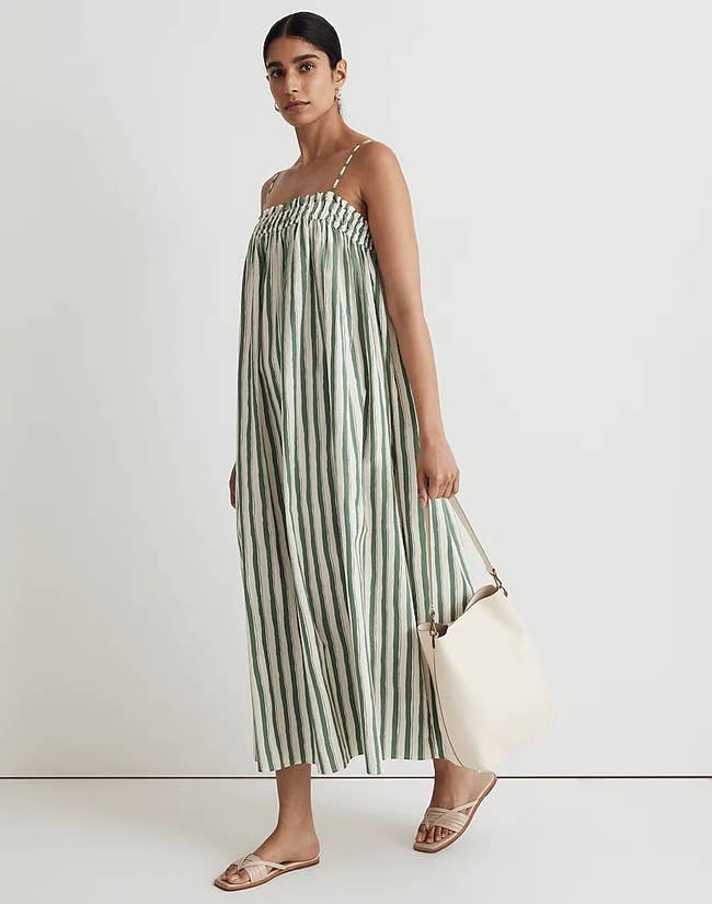 model in the green and white striped a-line midi dress and sandals while holding a purse