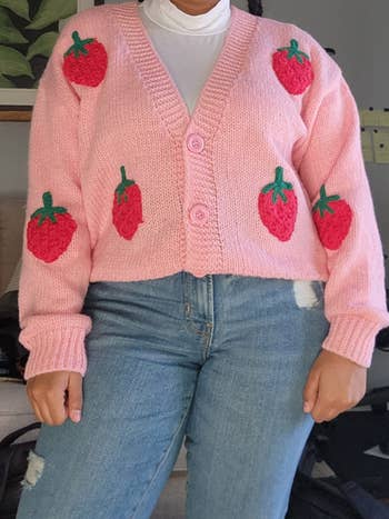 Person wearing a pink cardigan with strawberry patterns, paired with jeans and a white turtleneck