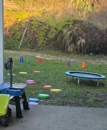 Backyard setup for kids with stepping stones, a tiny trampoline, and postulation cones surrounded by trees