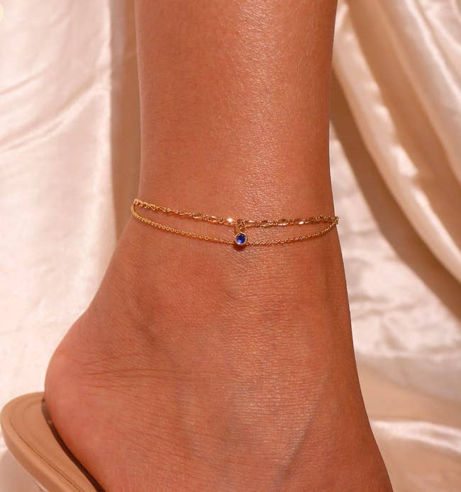 Model wearing double layer gold anklet with a small blue stone 