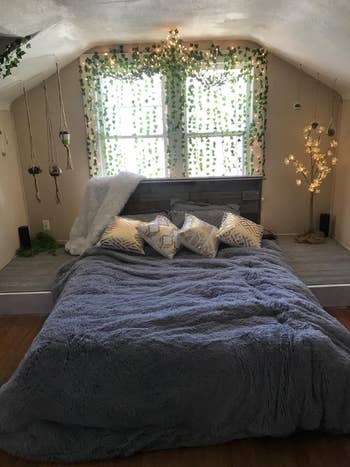 Cozy bedroom with a plush bedspread, decorative pillows, hanging plants, and fairy lights, creating a serene and inviting atmosphere